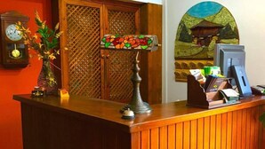 A reception desk with a clock, a vase of flowers, a stained glass lamp, and a painting on the wall. - Hotel Los Ángeles (Cabrales)