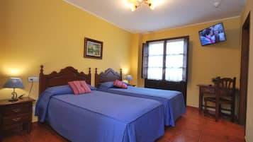 A bedroom with two beds, a TV on the wall, and a window with curtains.