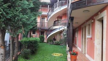 A courtyard with a green lawn, a tree, and a building with a balcony.