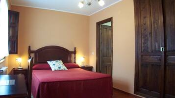 A bedroom with a wooden bed, two bedside lamps, a wooden wardrobe, and a door.