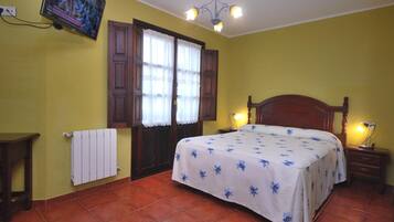 A bedroom with a bed, a television mounted on the wall, a radiator, and a window with curtains.