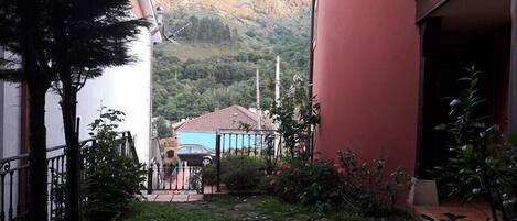 Un patio con un sendero de piedra, un coche aparcado al fondo y una montaña a lo lejos.