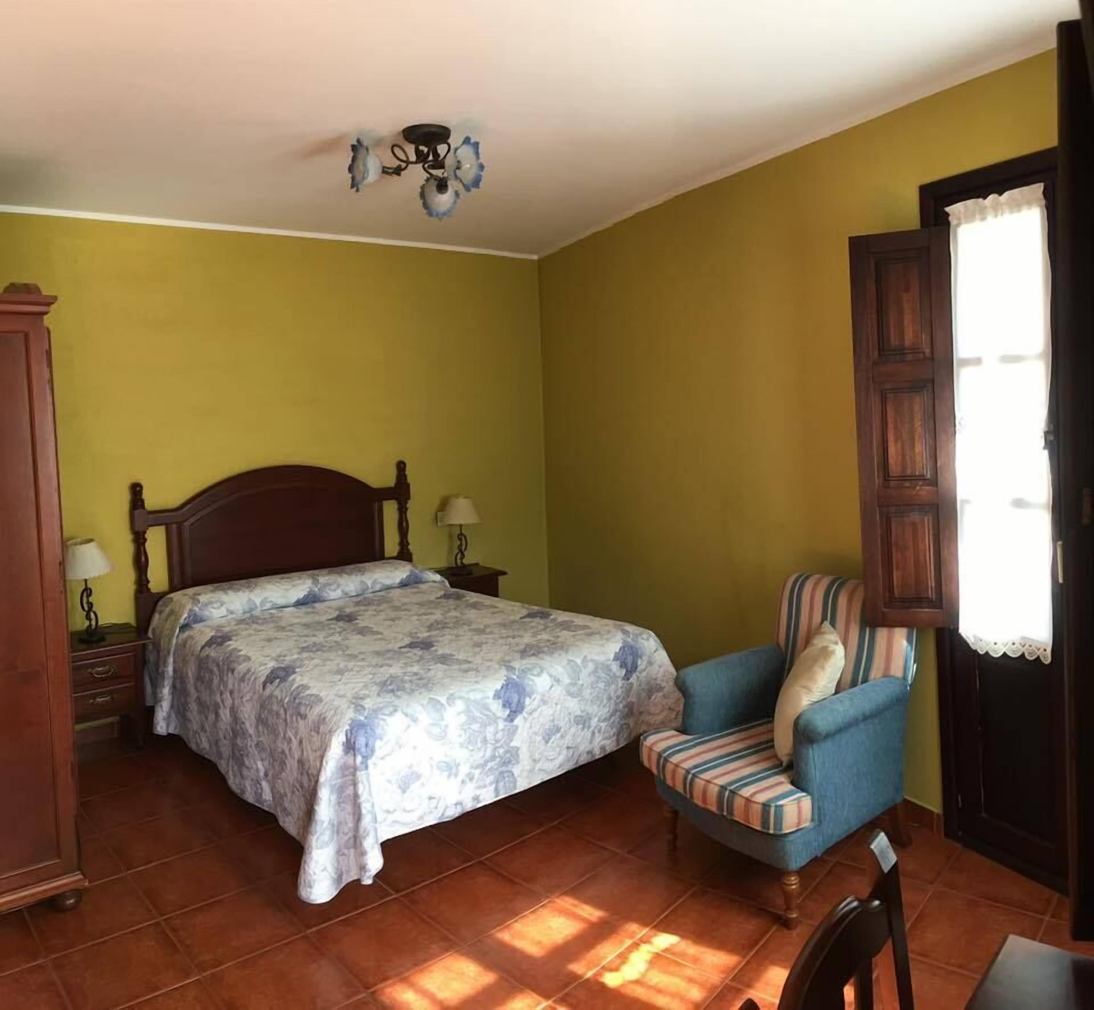 Un dormitorio con cama, una silla, una mesita de noche, una lámpara y un armario.