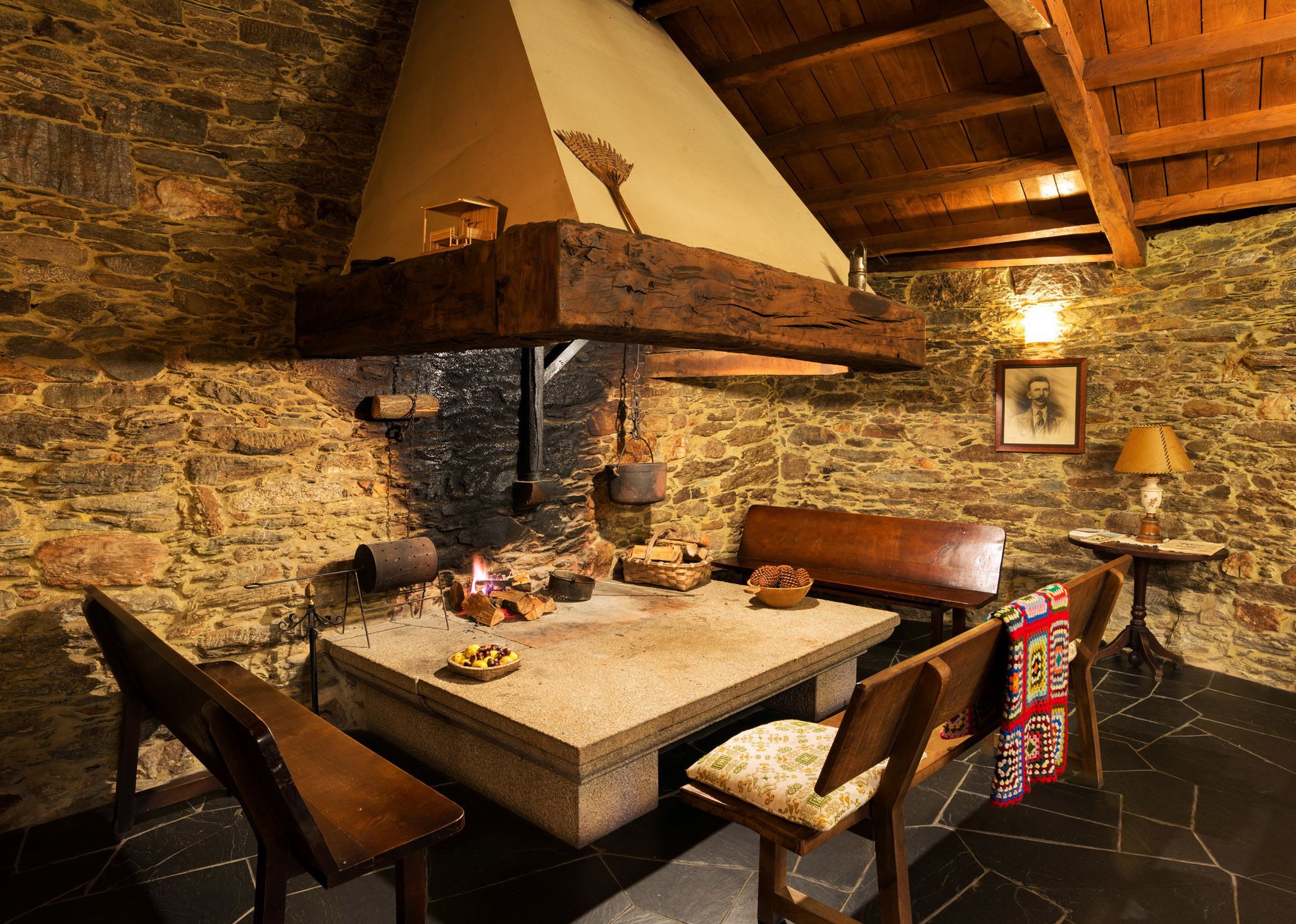 Una habitación de paredes de piedra con chimenea de piedra, muebles de madera y un banco.
