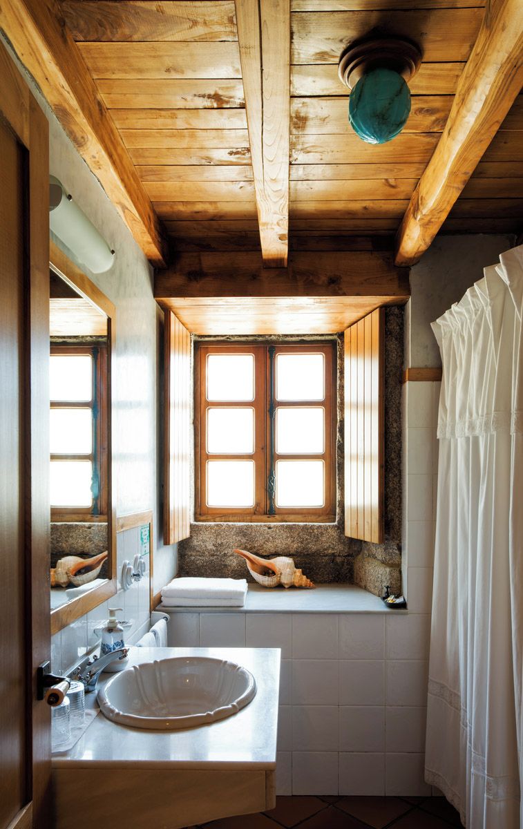 A bathroom with a wooden ceiling, a window with a view, a sink, and a towel rack.
