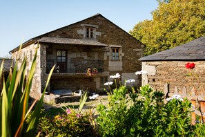 A stone building with a balcony, surrounded by lush greenery and flowers. - Casa Lourán (Monfero)