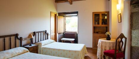 Una habitación con dos camas, techo de madera, una mesita con una silla, un armario y una ventana con vistas.