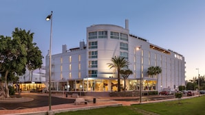 A modern hotel with a curved facade, multiple balconies, and a well-lit entrance.
