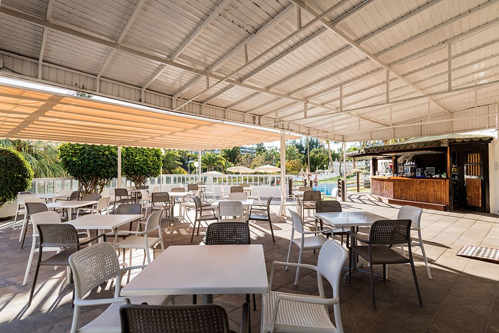 Un patio exterior con mesas, sillas, piscina y bar.