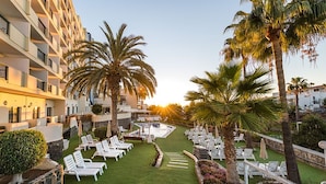 A hotel courtyard with a swimming pool, palm trees, and sun loungers.