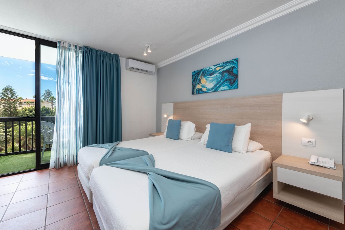 A hotel room with a large bed, a nightstand, a view of the outdoors, and a painting on the wall.