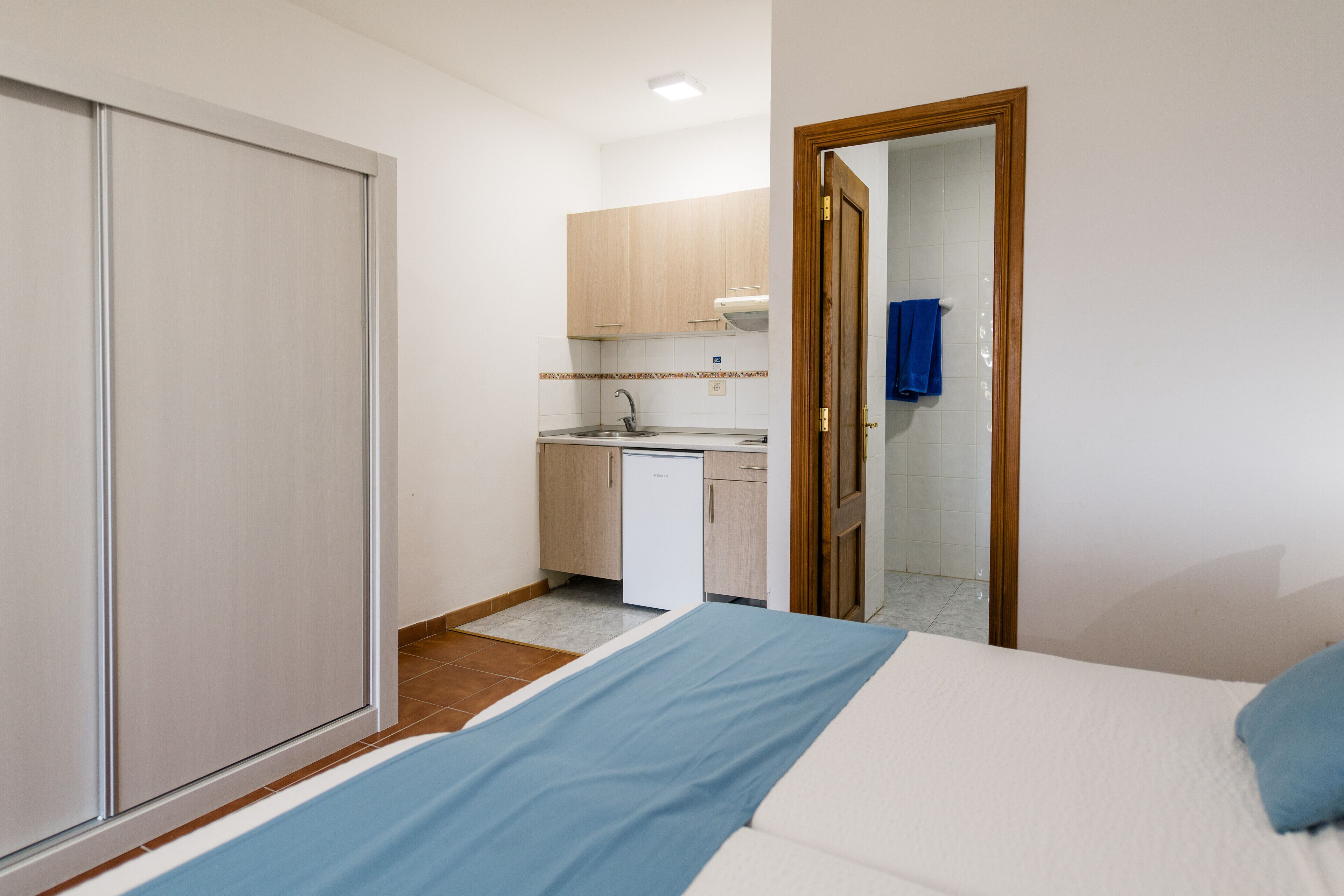 A small, compact room with a bed, a kitchenette, and a bathroom.