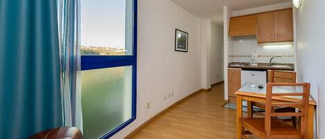 A compact living space with a kitchenette, a dining area with a table and chairs, and a large window with curtains.