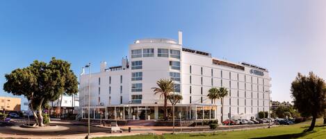 A modern hotel with a curved facade, multiple floors, and a covered entrance area with palm trees.