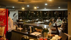 Un restaurante con varias mesas y sillas, una zona de bar con mostrador y distintos objetos encima, y lámparas colgantes.