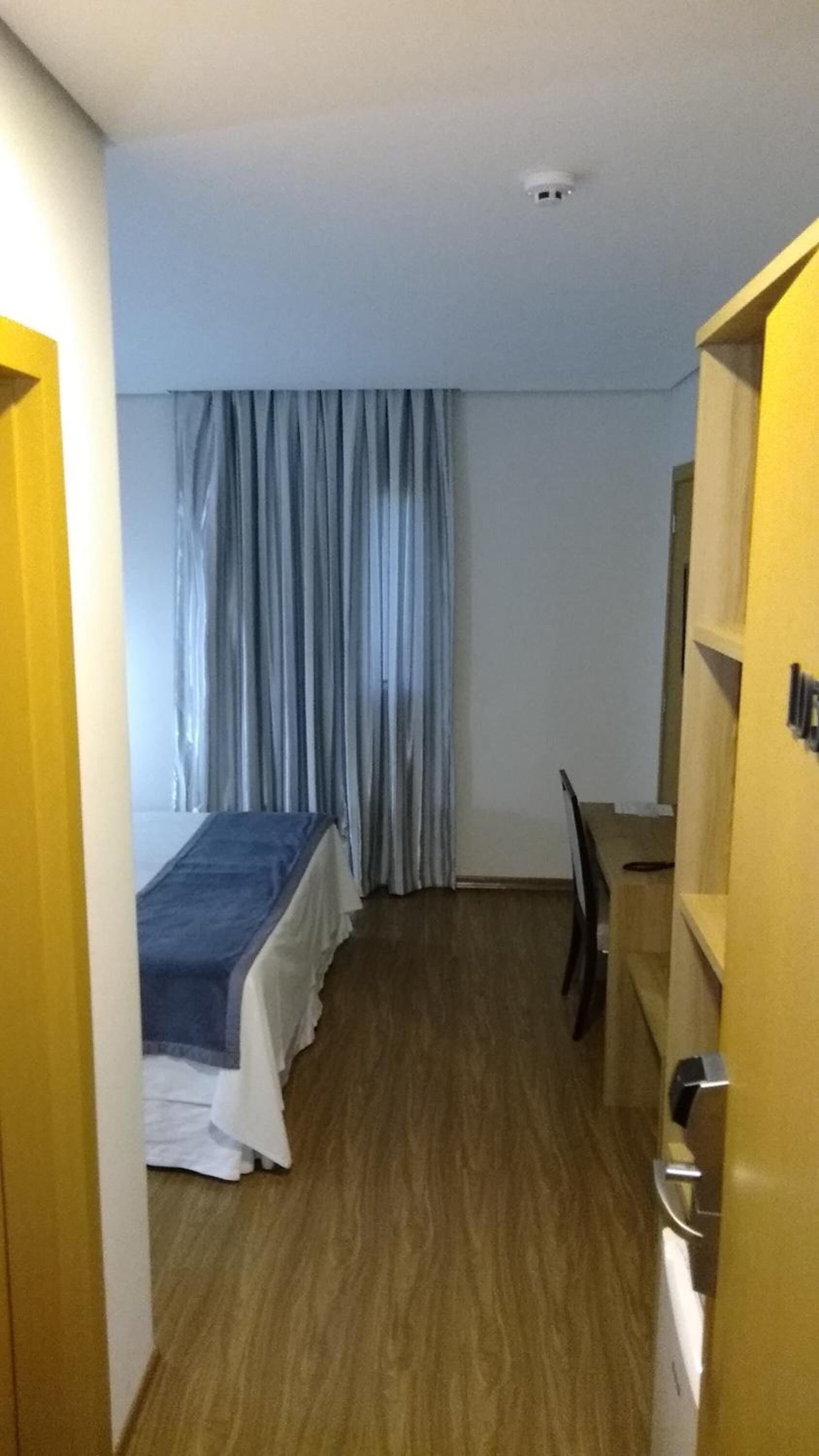 A small, narrow room with a bed, a desk, and a chair.
