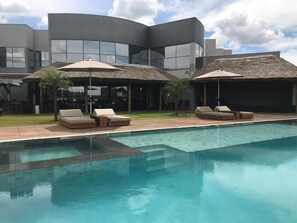 A modern hotel with a swimming pool, lounge chairs, and thatched umbrellas.