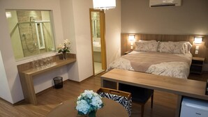 Una habitación de hotel con cama, mesitas de noche, escritorio, silla, una pequeña mesa con flores, espejo y ventana.