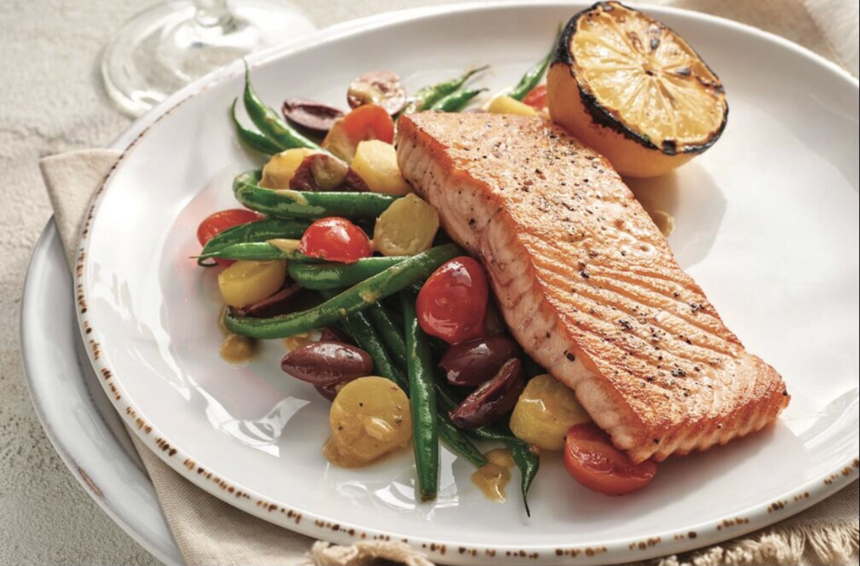 Une assiette contenant du saumon grillé, des tomates cerises, des haricots verts et des tranches de citron.