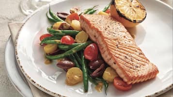 Une assiette contenant du saumon grillé, des tomates cerises, des haricots verts et des tranches de citron.