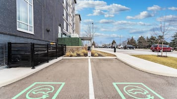 A parking lot with electric vehicle charging stations, a building with a black exterior, and a clear sky.