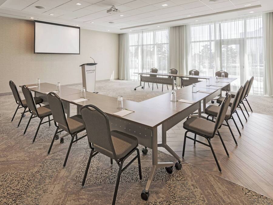 Un salón de conferencias con una larga mesa, sillas, un atril y una pantalla para proyector.
