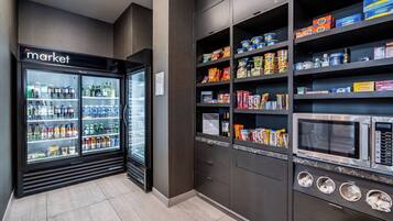 Een kitchenette met een koelkast vol drankjes, een magnetron, en planken met snacks en toevoegingen.
