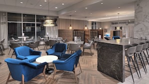 A modern hotel lobby with a central seating area, a bar, and a large window providing a view of the city. - Courtyard by Marriott Burlington (Burlington)