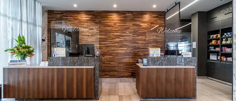 A modern hotel reception area with two reception desks, a wooden wall, and a 'Welcome' sign.