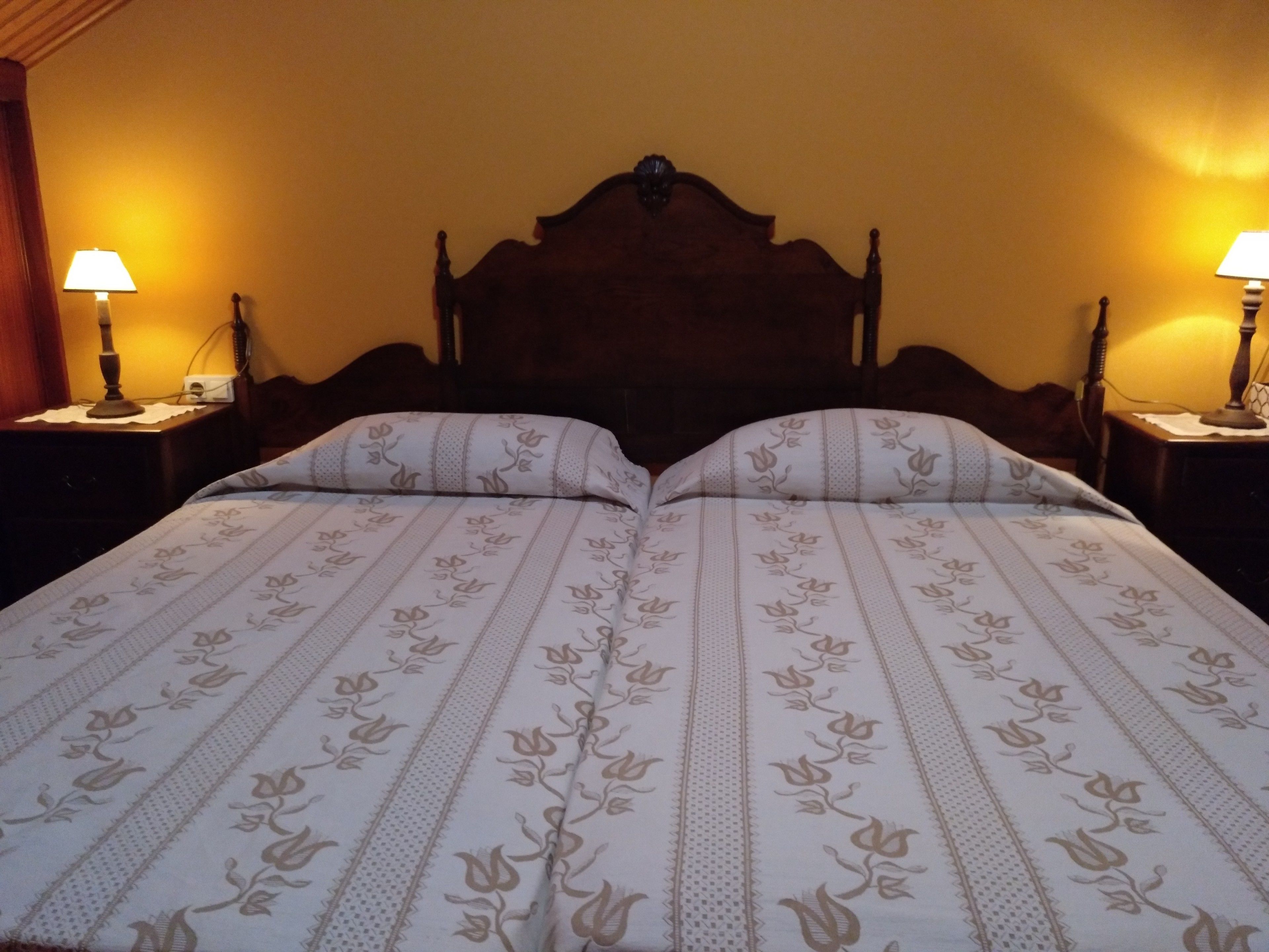A double bed with a floral-patterned bedspread, two bedside tables with lamps, and a wooden headboard.