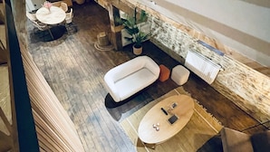 A modern interior with a wooden floor, a sofa, a dining table with chairs, and a hanging light fixture.