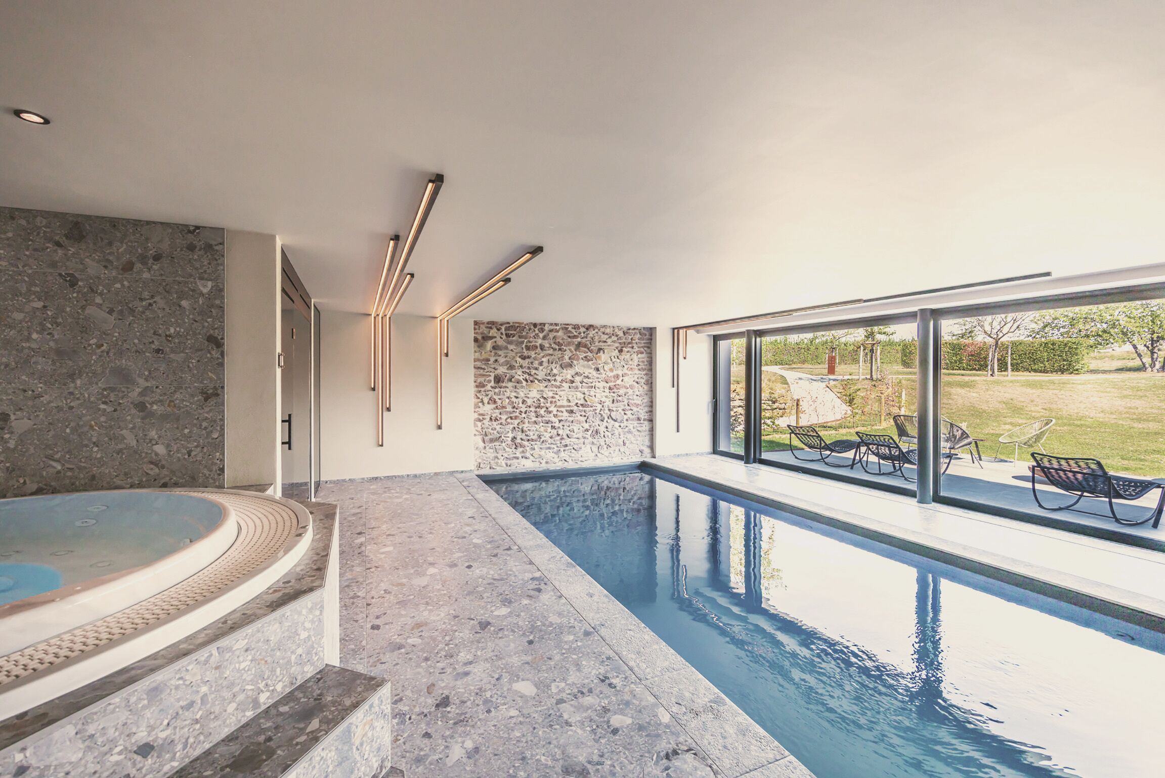 Piscina interior moderna com parede de pedra e área de hidromassagem.