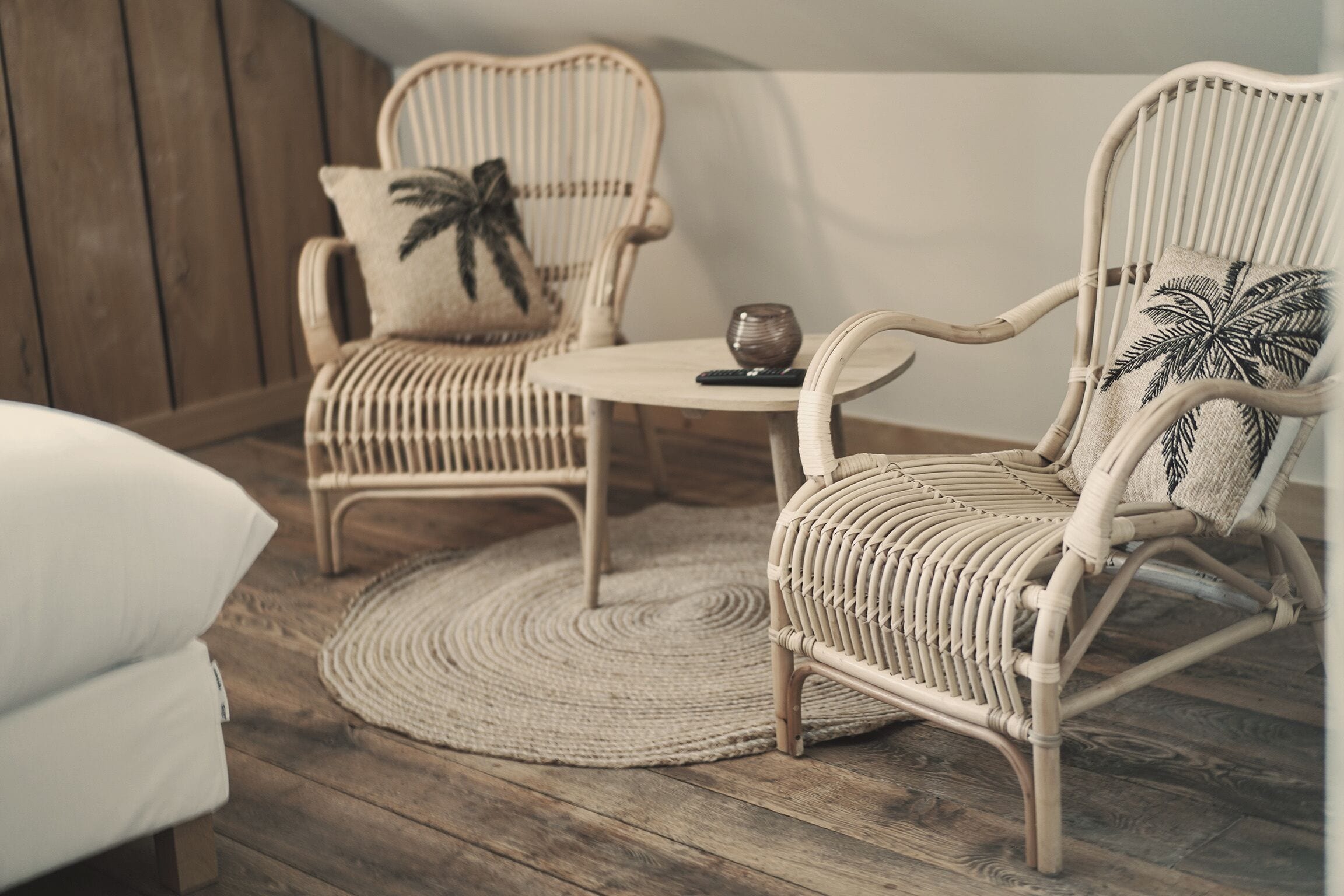 Une pièce comprenant deux fauteuils en osier, une petite table ronde et un tapis tissé posé sur un plancher en bois.