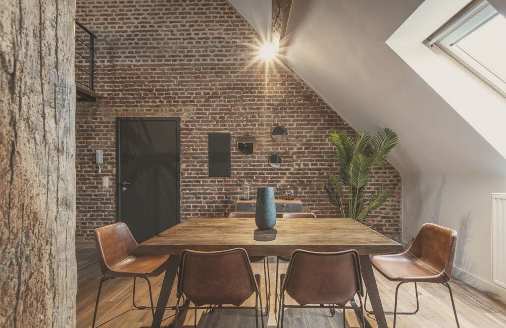 Un comedor con pared de ladrillo, una ventana grande y una mesa de madera con sillas.