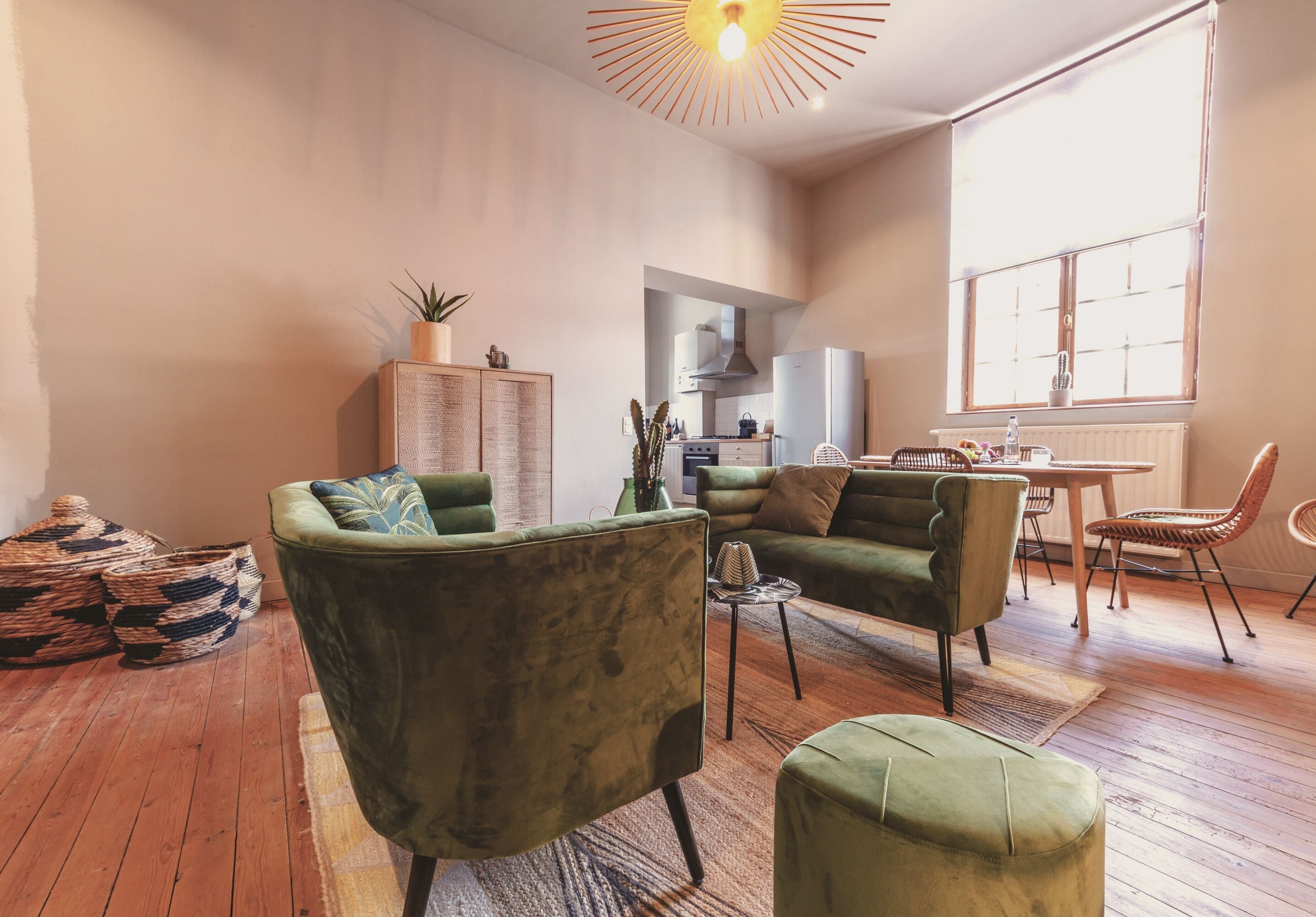 A spacious living room with a sofa, armchair, and ottoman, a kitchen area, and a dining table with chairs.