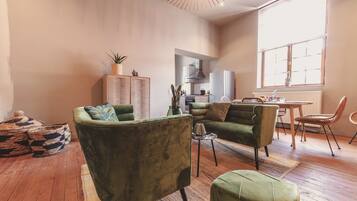 A spacious living room with a sofa, armchair, and ottoman, a kitchen area, and a dining table with chairs.