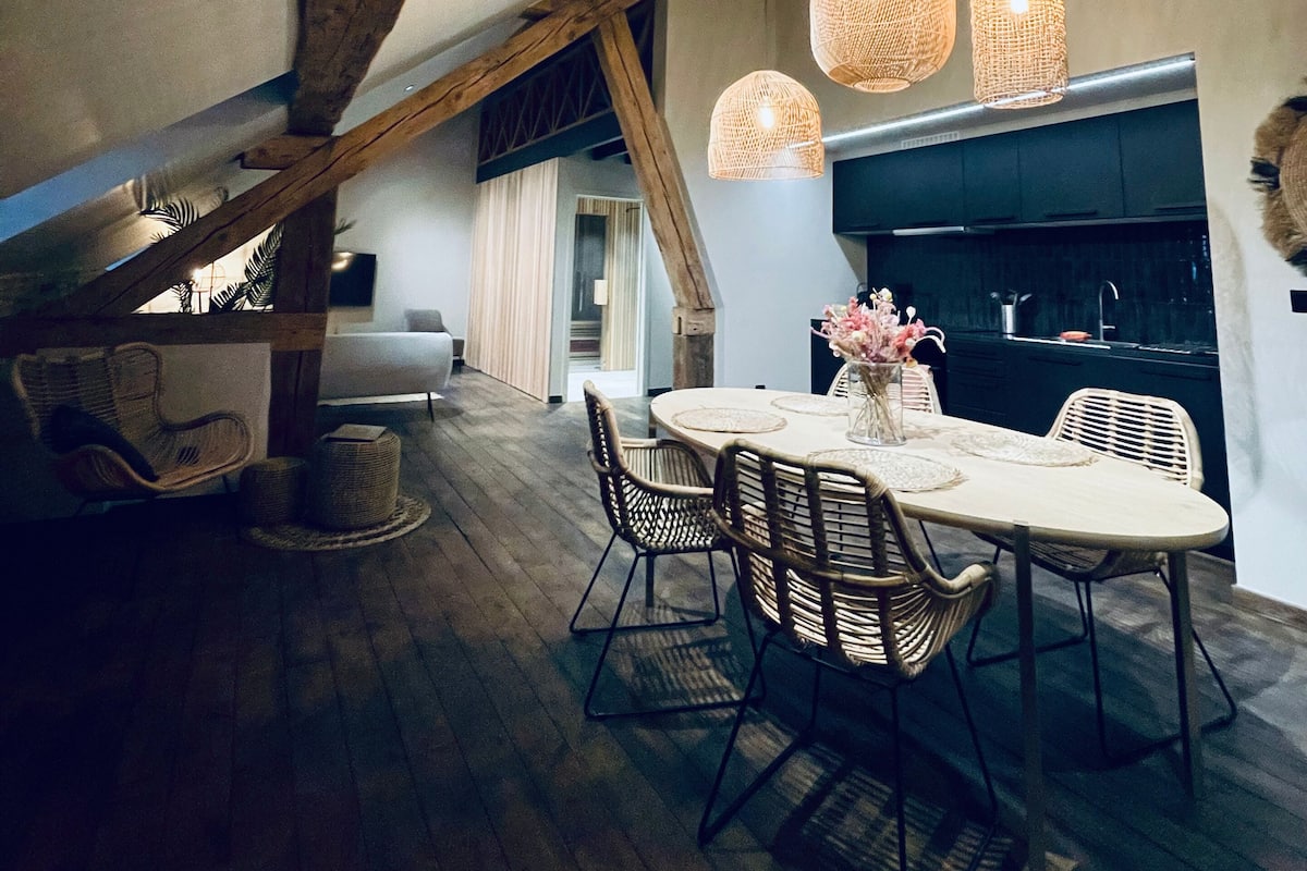 Un coin repas avec une table ronde, des chaises en osier et des suspensions en osier.