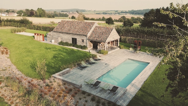 A large house with a swimming pool, surrounded by a well-maintained lawn and a view of the countryside.