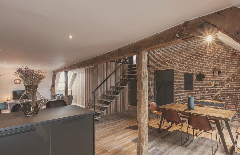 Een moderne keuken met een centraal eiland, een eethoek met een houten tafel en stoelen, en een trap naar een hoger niveau.