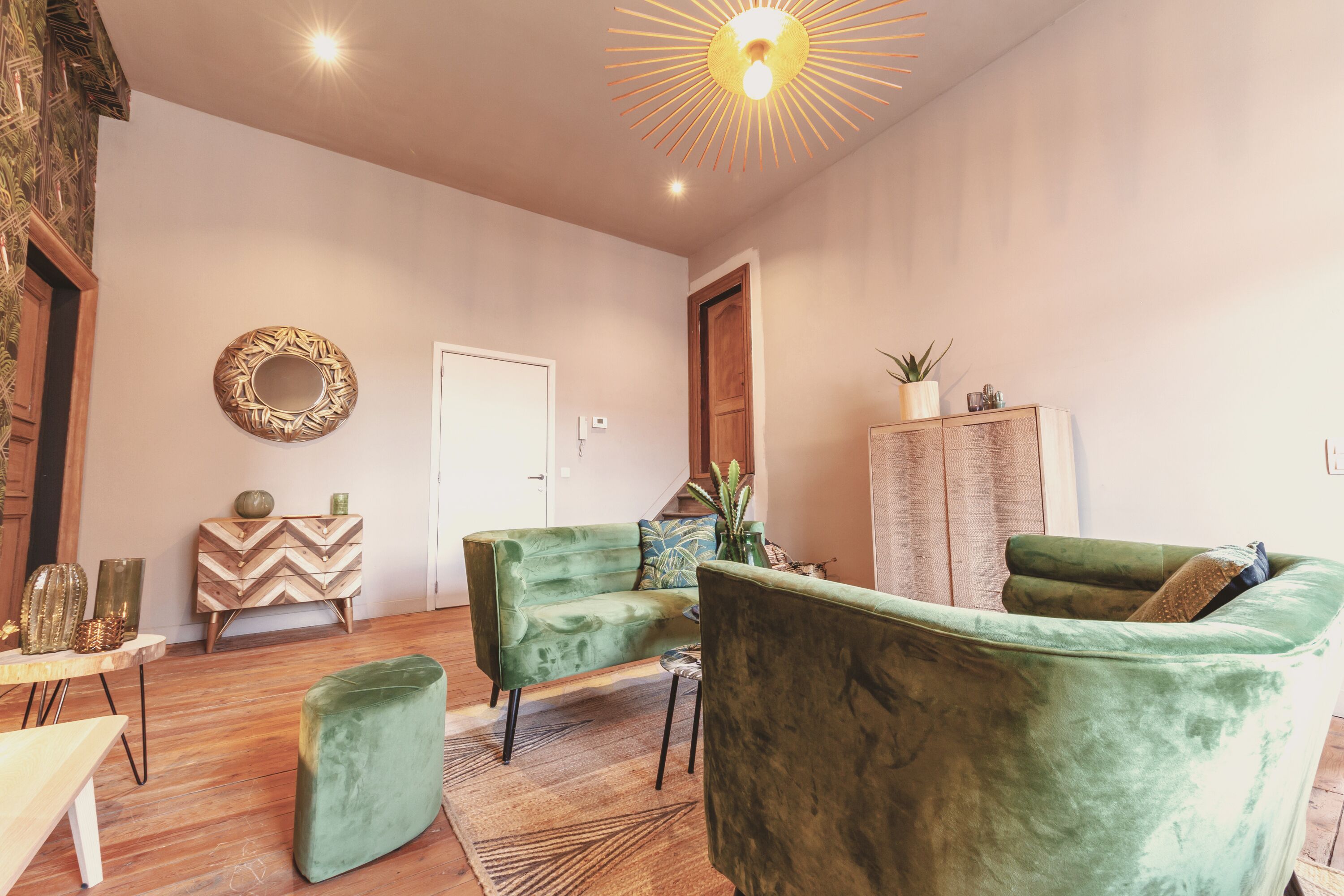 Een ruime woonkamer met een groene bank, een bijpassend voetenbankje en een houten kast.