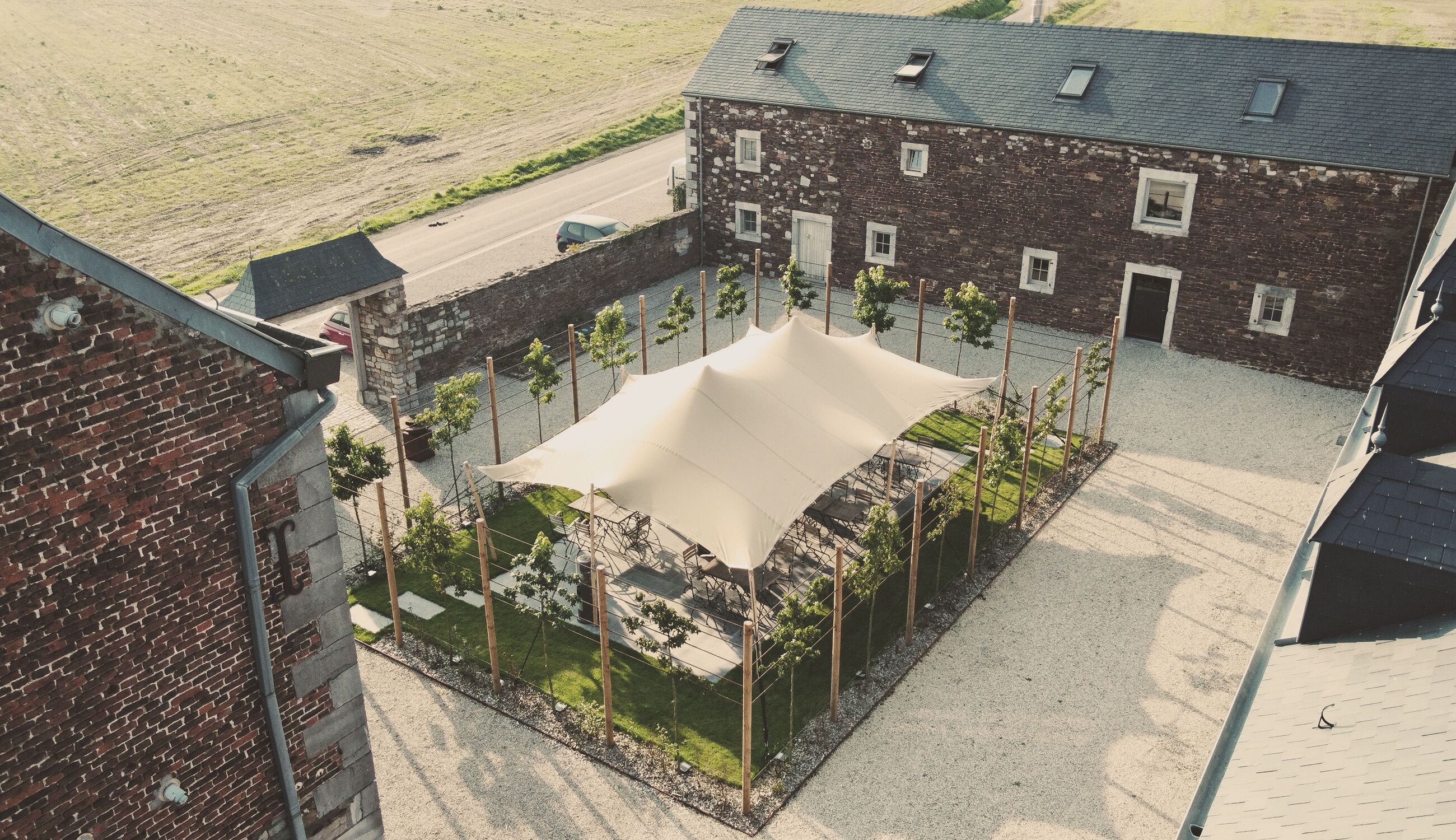 A courtyard with a large tent, surrounded by brick buildings and a grassy field.