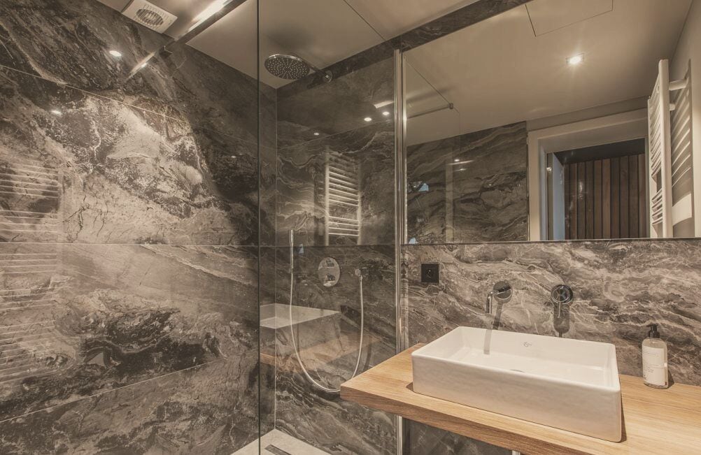 Et moderne badeværelse med en marmorbeklædt bruseniche, et glasafskærmet brusebad og en trækommode med vask.