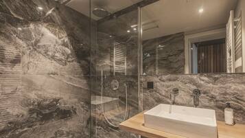 Et moderne badeværelse med en marmorbeklædt bruseniche, et glasafskærmet brusebad og en trækommode med vask.