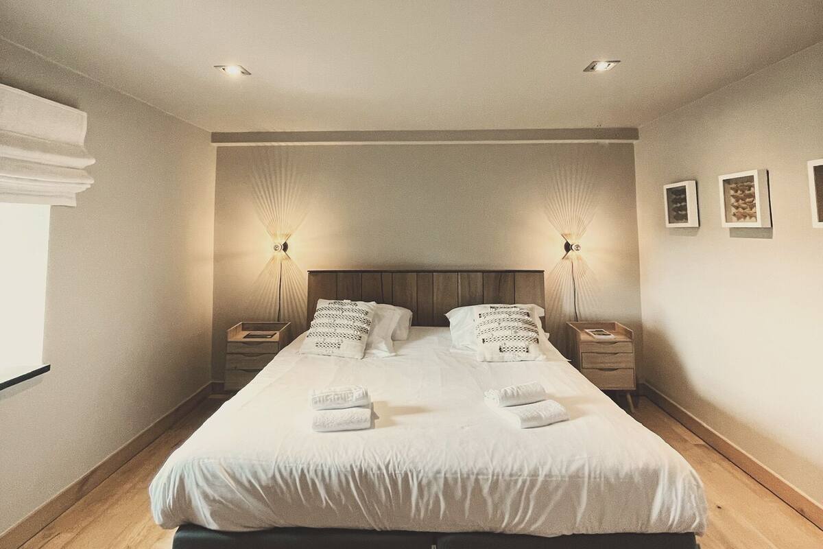 Une chambre d’hôtel moderne avec un grand lit, deux tables de chevet et une petite table d’appoint.
