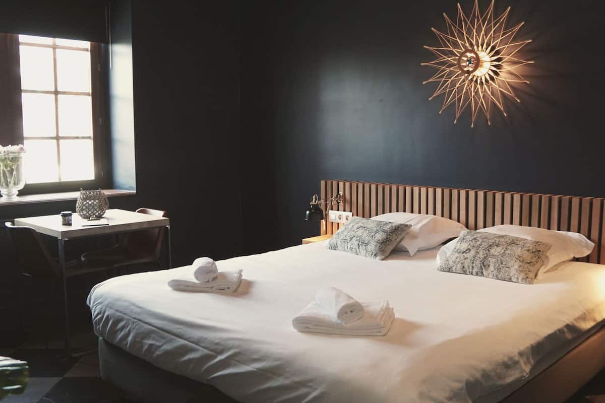 Un lit bien fait, avec des serviettes, une table de chevet avec une lampe et un luminaire mural en forme d’étoile.