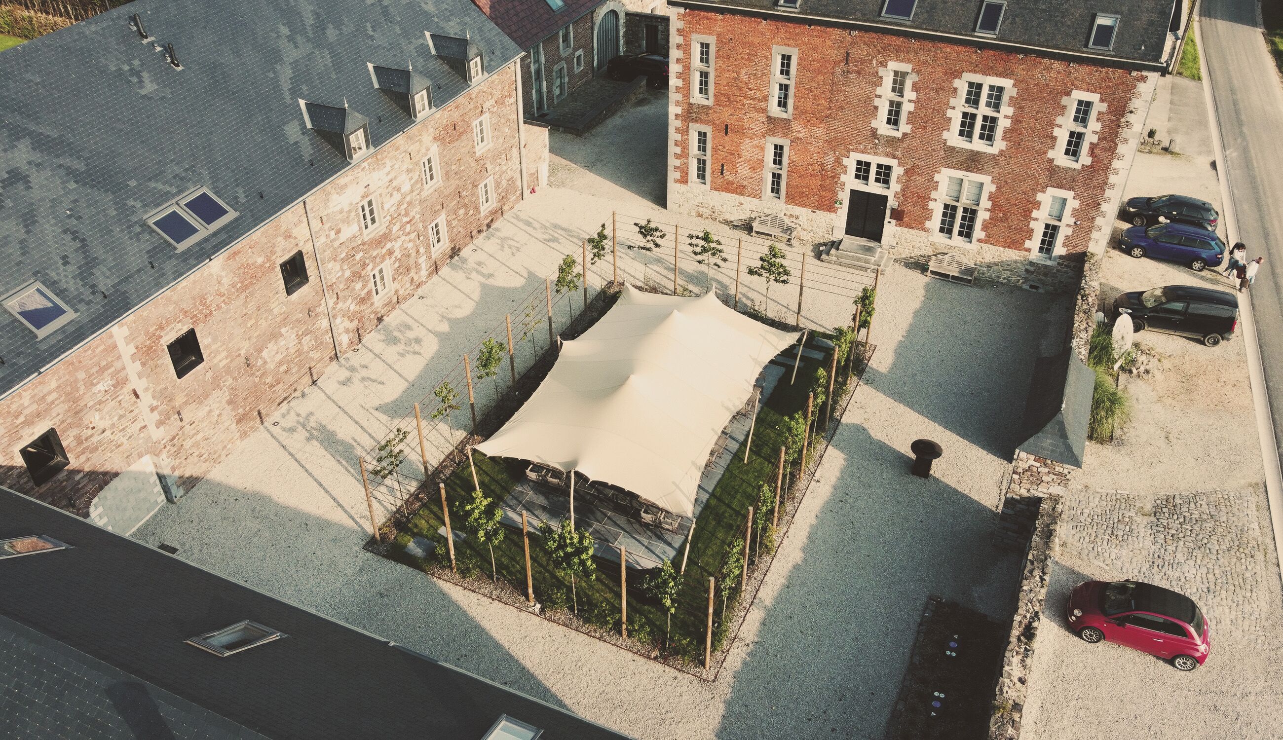 Vue aérienne d’une cour intérieure avec un espace de repos abrité, des bâtiments en briques et des voitures garées.