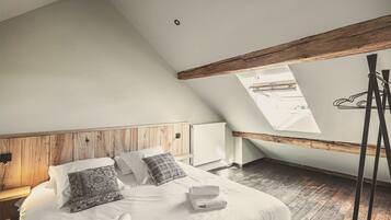Een slaapkamer met een schuine kap, houten balken, een bed met witte lakens, een dakraam en een radiator.