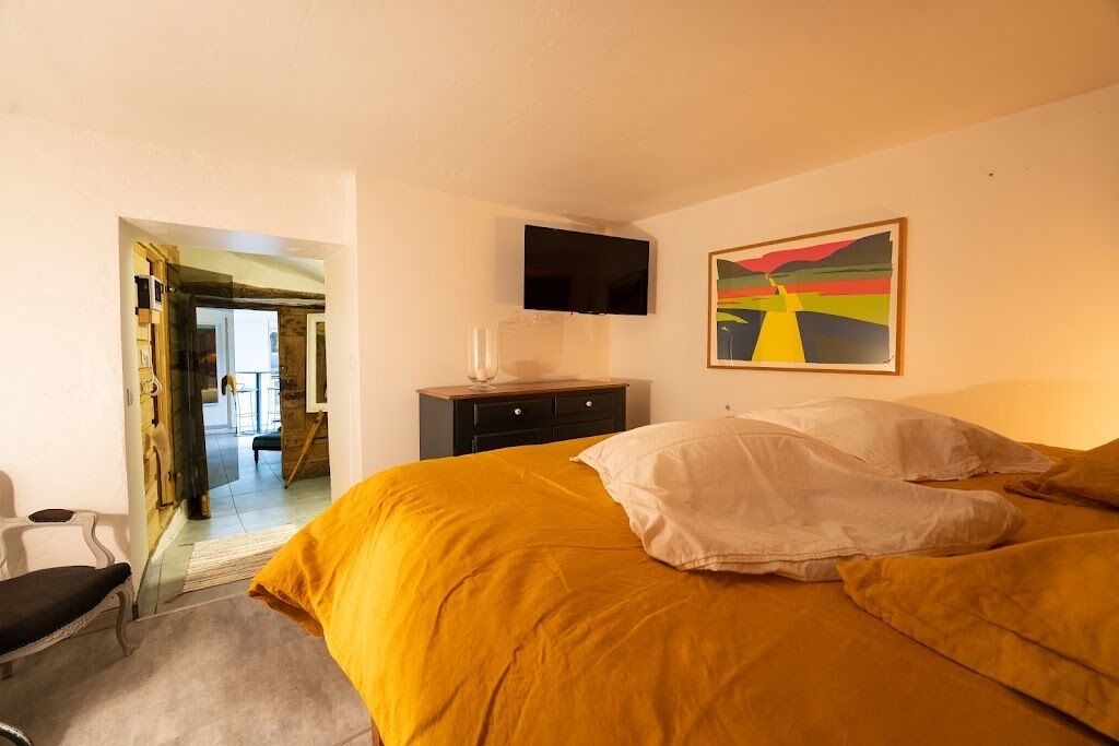 A hotel room with a bed, a TV on the wall, and a painting.