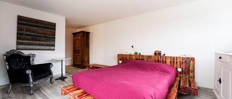 A bedroom with a wooden bed frame, a black chair, a small white table, and a wooden wardrobe.
