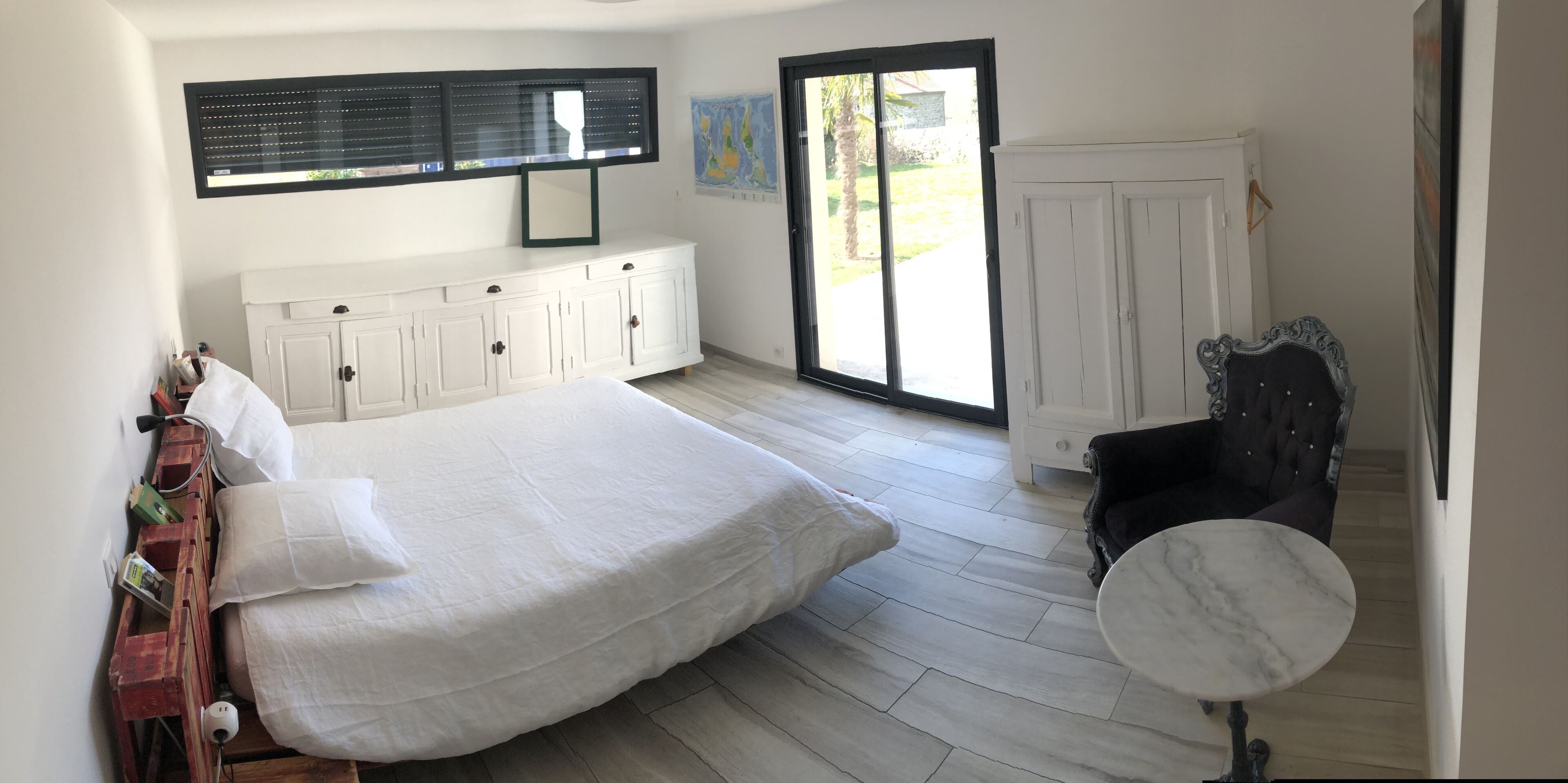 A bedroom with a bed, a white dresser, a black chair, and a small round table.